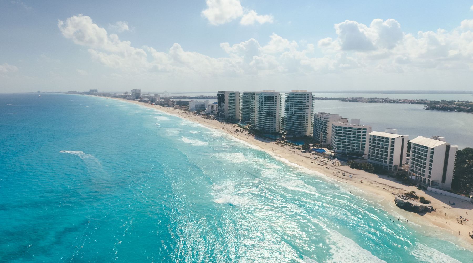 Aerial view of the Cancún Hotel Zone: a line of high-rise hotels along a white beach, turquoise sea on one side and the lagoon on the other.